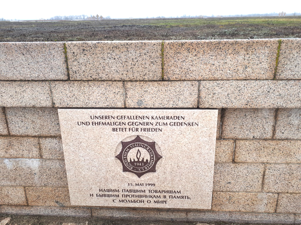 A memorial plate on the German side of the cemetery with the inscription in German and Russian: "To Our Fallen Comrades and Former Foes in Memory of the Prayer for Peace" A memorial plate on the German side of the cemetery with the inscription in German and Russian: "To Our Fallen Comrades and Former Foes in Memory of the Prayer for Peace"